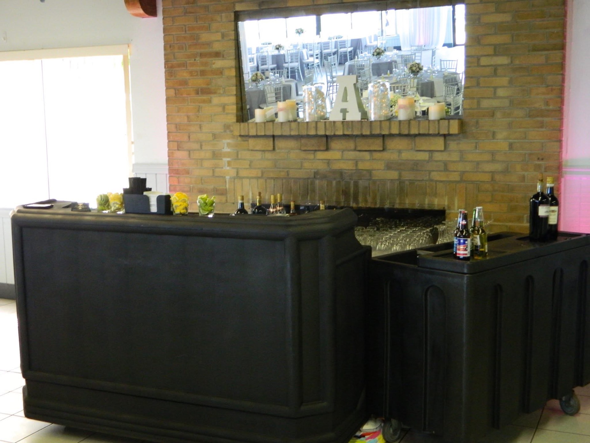 Two black portable bars set up beside a brick fireplace at a reception venue